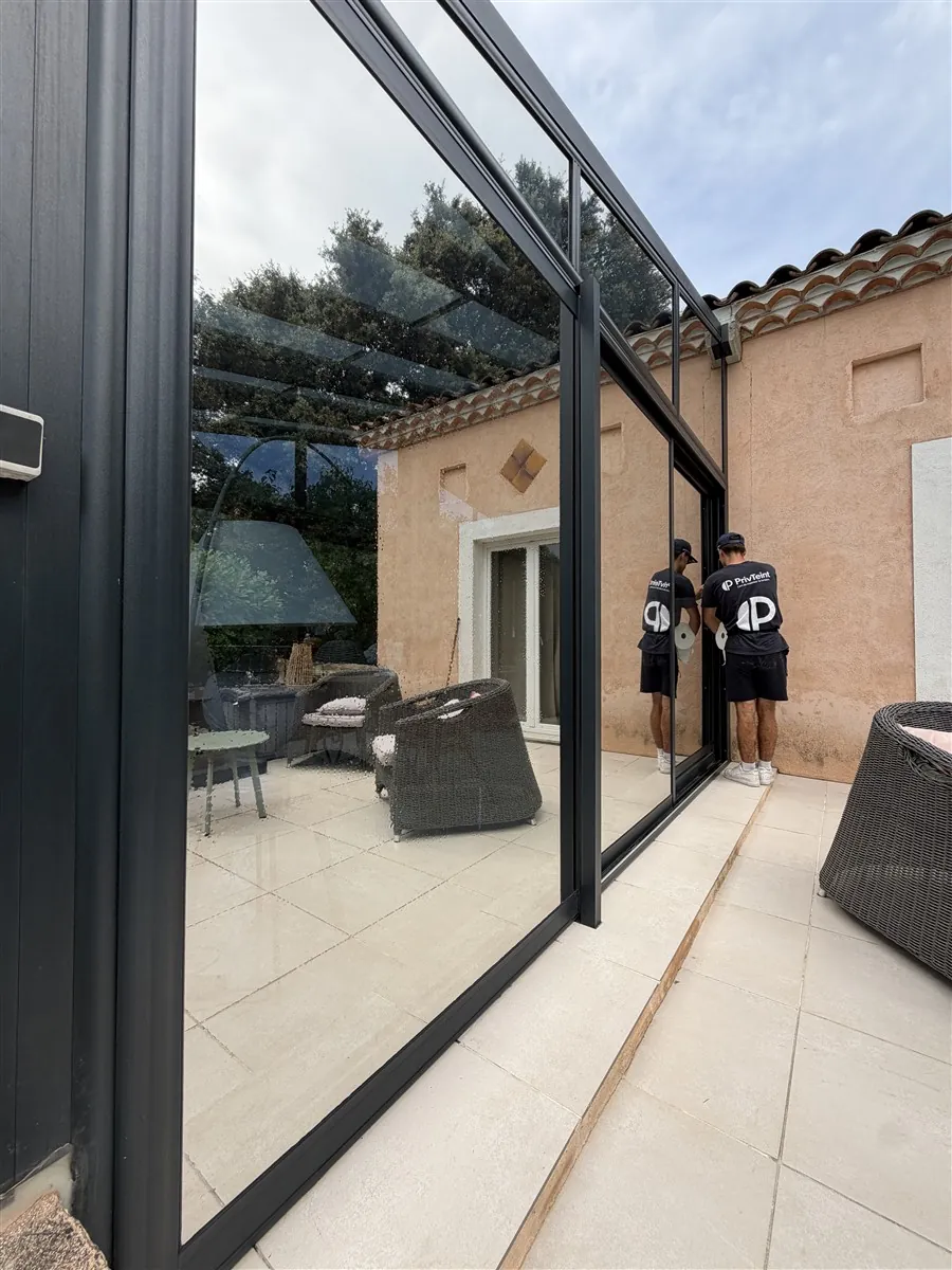 Deux techniciens PrivTeint posant un film solaire sur une véranda vitrée avec vue terrasse à Hyères