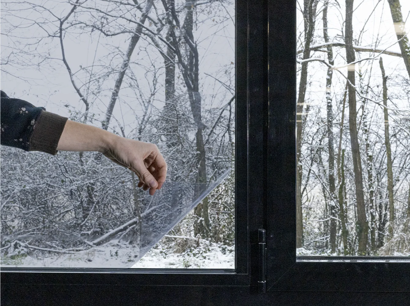 Application d'un film basse émissivité transparent sur une fenêtre, avec un paysage enneigé derrière la vitre