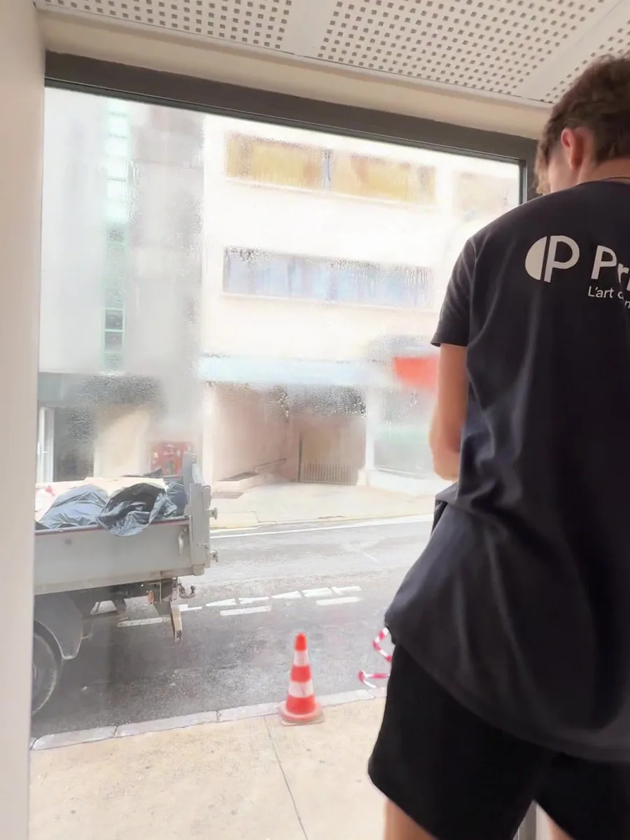 Avant la pose : la vitrine d'angle du local commercial est transparente, la rue et les immeubles d'en face sont entièrement visibles depuis l'intérieur.