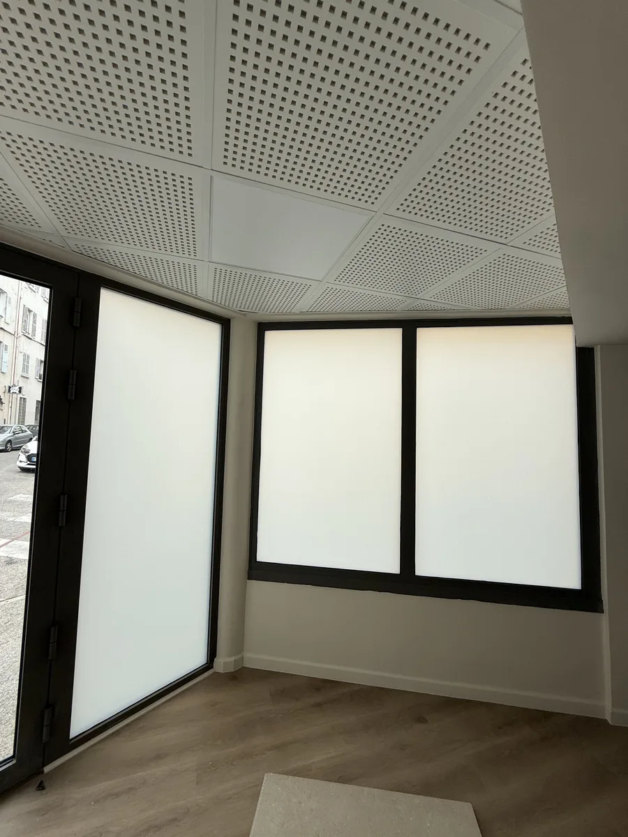 Intérieur du local commercial à Hyères après la pose : angle de baies vitrées en film dépoli blanc, lumière diffuse dans la pièce.