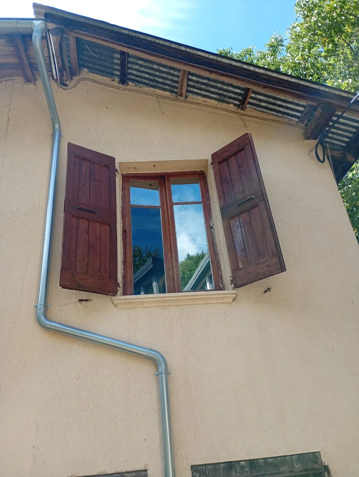Fenêtre à volets bois vue de l’extérieur après pose d’un film miroir sans tain : le vitrage renvoie le ciel