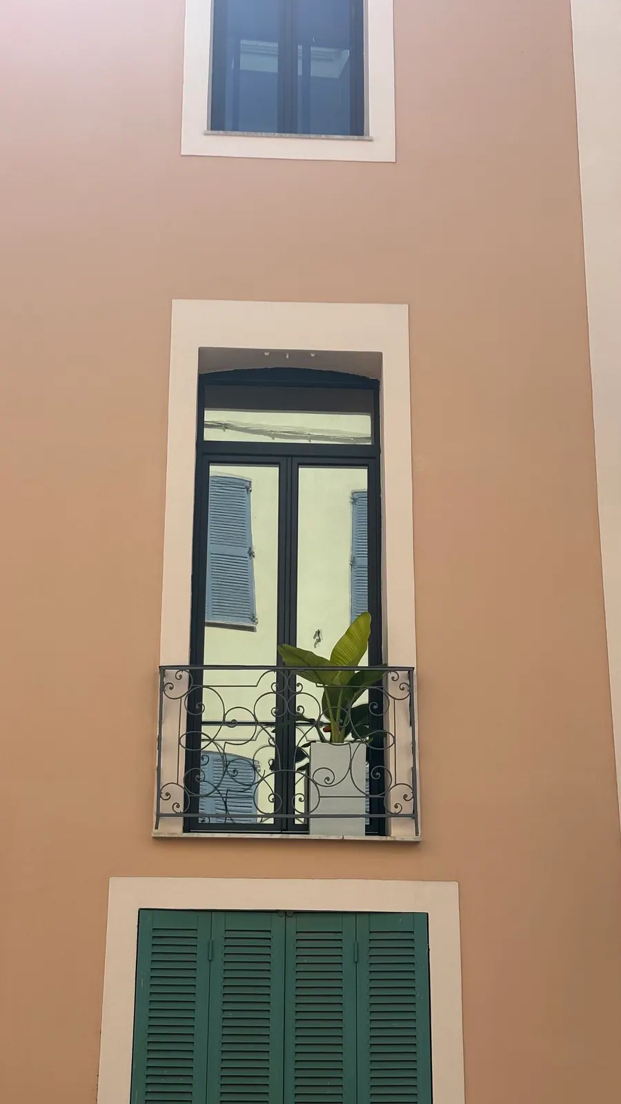 Film miroir sans tain posé par PrivTeint sur une porte-fenêtre à garde-corps en fer forgé à Saint-Raphaël : reflet des volets bleus d'en face, intérieur invisible