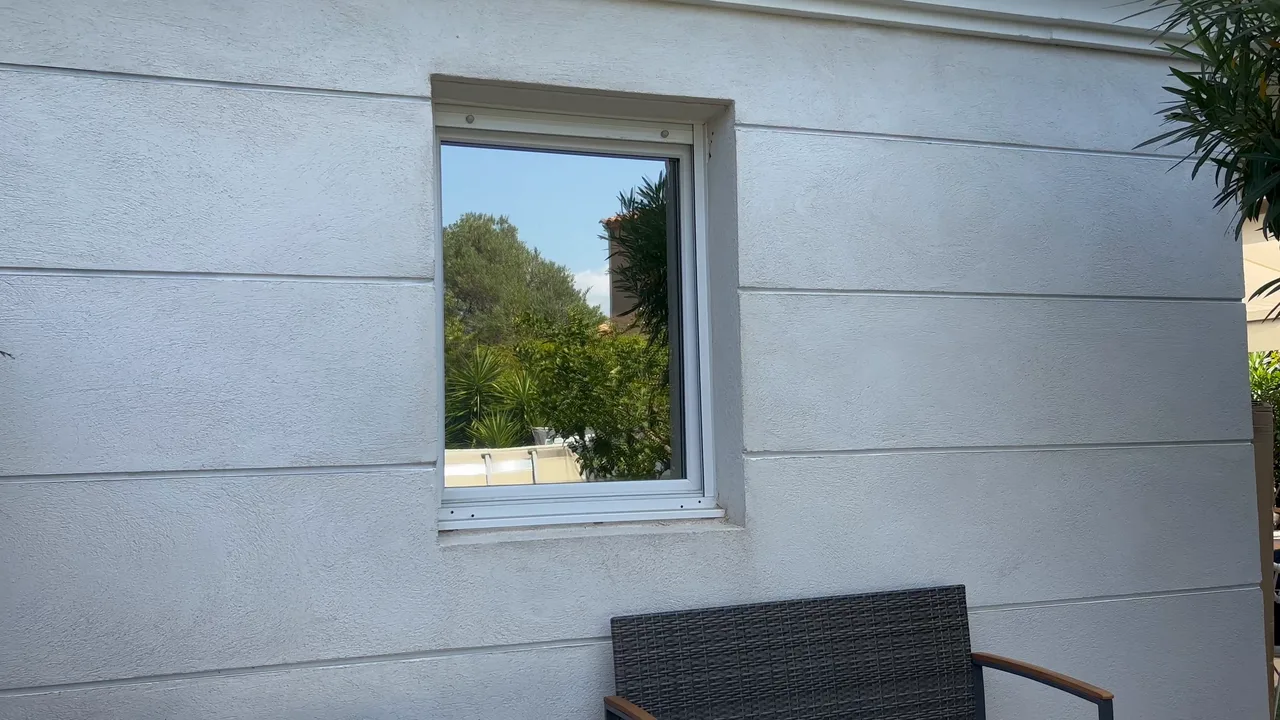 Fenêtre de chambre équipée d'un film miroir sans tain à Hyères : depuis la terrasse, le vitrage renvoie les arbres et le ciel.