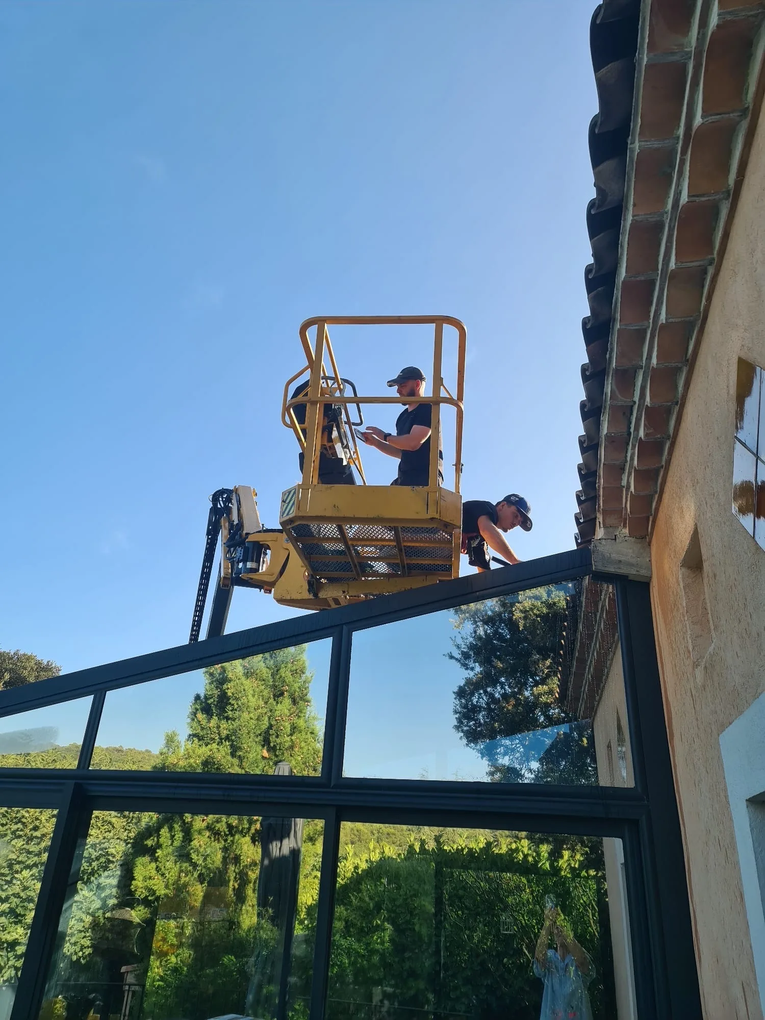 Vue depuis le panier de la nacelle sur une véranda vitrée et le jardin d’une bastide varoise