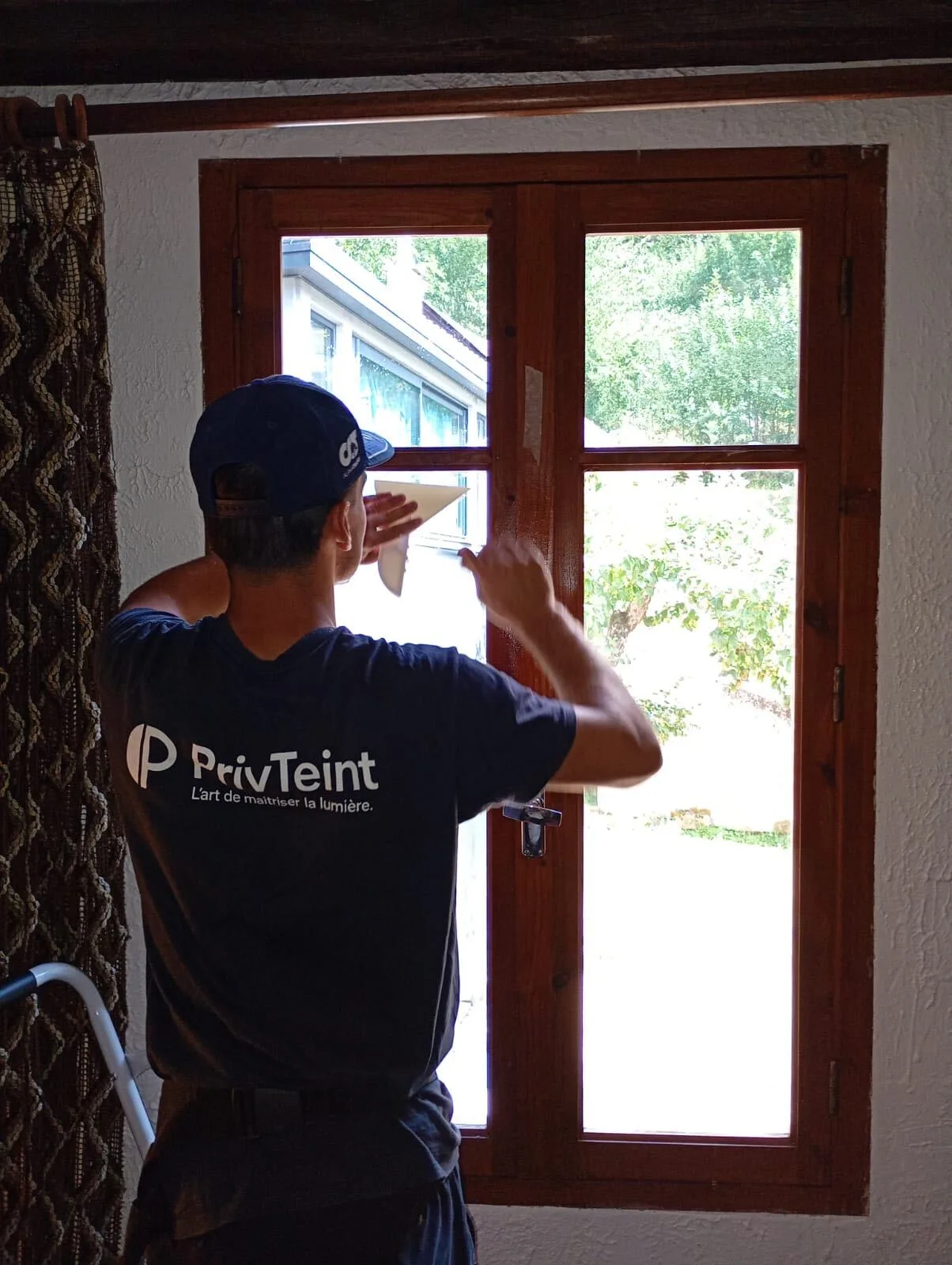 Technicien PrivTeint posant un film miroir sans tain sur une fenêtre en bois, vue de l’intérieur