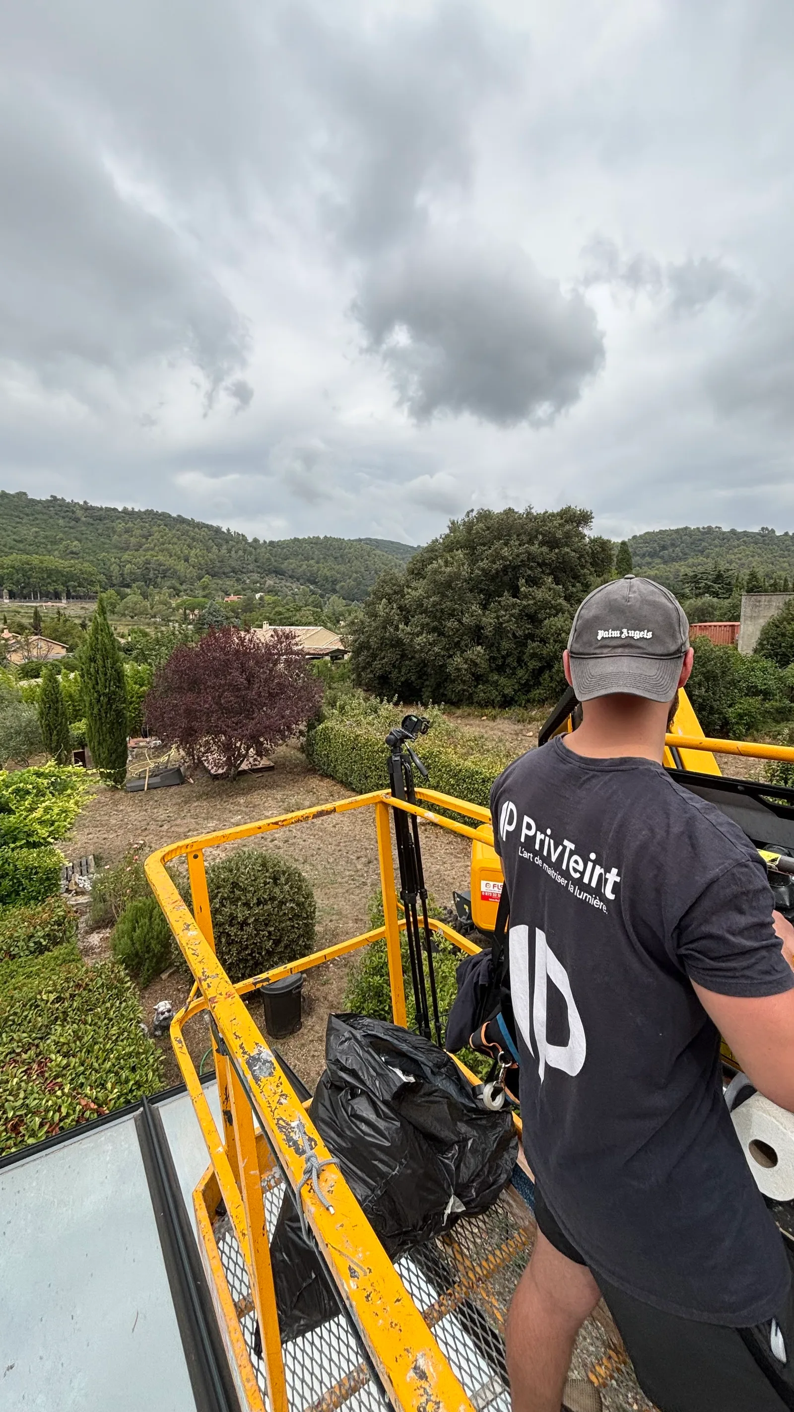 Technicien PrivTeint en nacelle au-dessus d’une toiture de véranda, piscine et jardin en contrebas